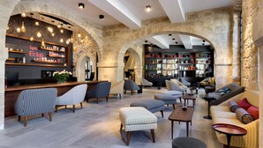 A spacious lobby with a bar area, seating arrangements, and a stone archway. - Boutique Hôtel des Remparts (Aigues-Mortes)