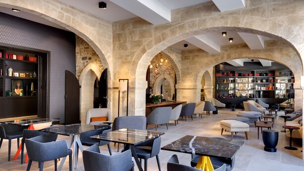 A spacious indoor area with stone arches, modern seating, and a bar area with shelves. - Boutique Hôtel des Remparts (Aigues-Mortes)