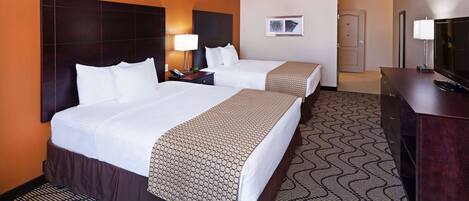 A hotel room with two beds, a TV, a desk, and a door leading to another room.