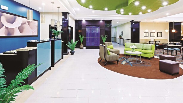 A modern lobby with a reception desk, seating area, and a green accent wall. - La Quinta Inn & Suites by Wyndham Marshall (Marshall)