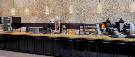 A self-service breakfast bar with various food items, coffee machines, and condiment dispensers.