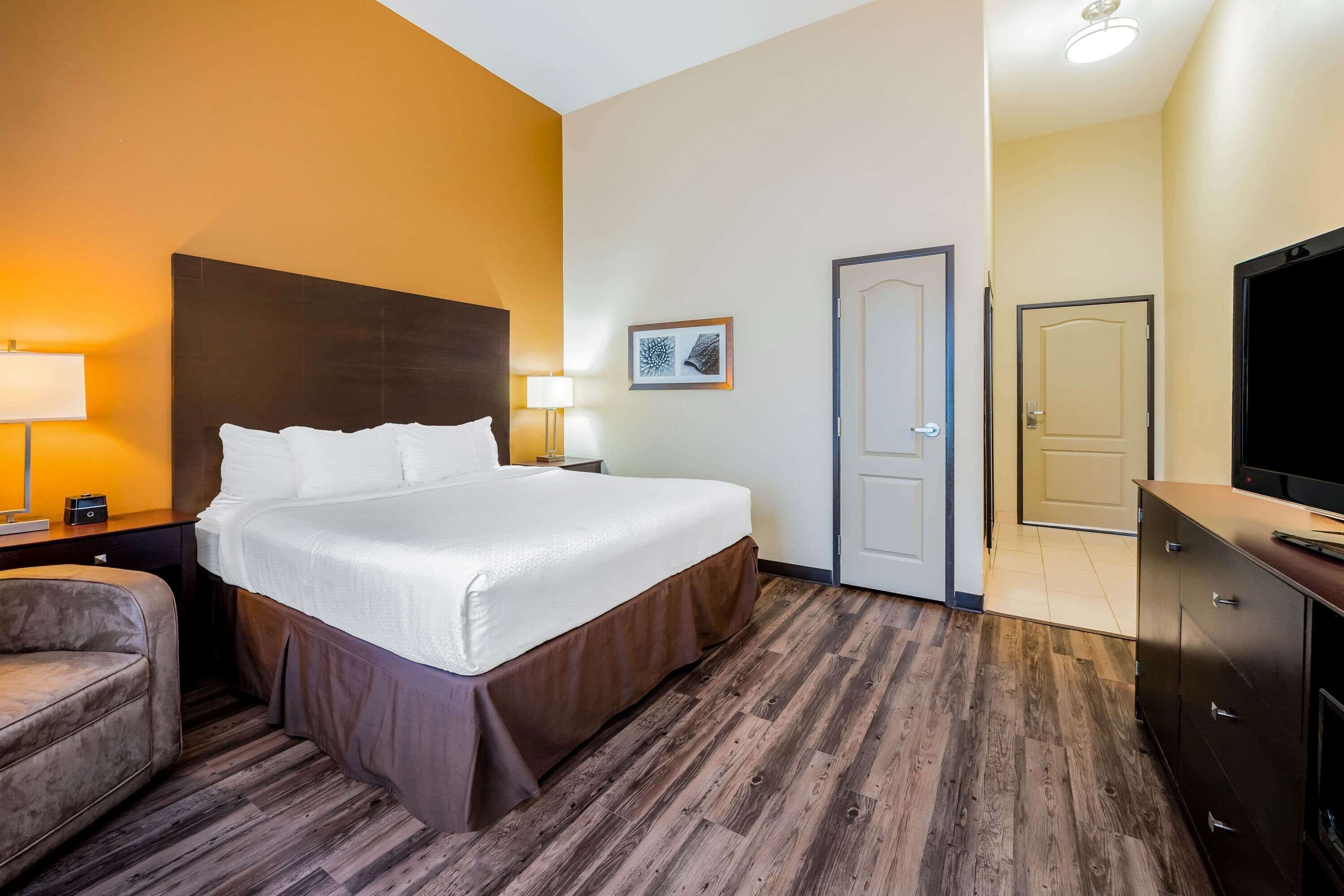 A hotel room with a large bed, two bedside lamps, a chair, a television, and a door.