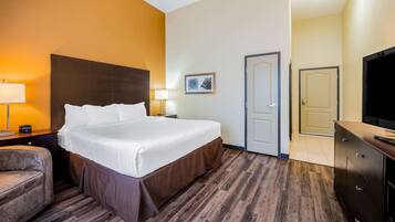 A hotel room with a large bed, two bedside lamps, a chair, a television, and a door.