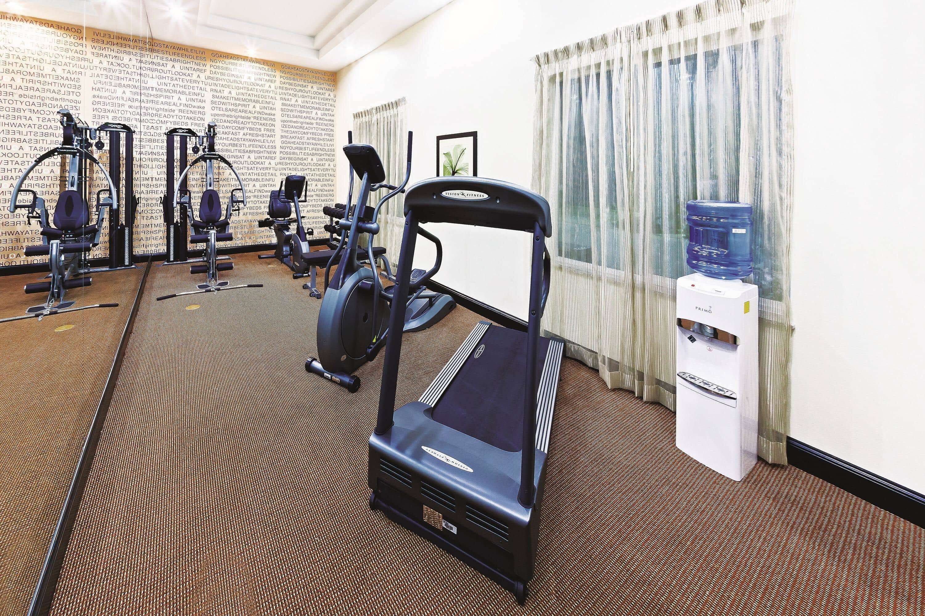 A hotel gym with treadmills, elliptical machines, and a water dispenser.