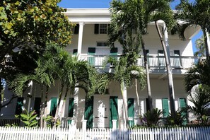 Un edificio bianco con persiane verdi e un recinto di legno bianco.