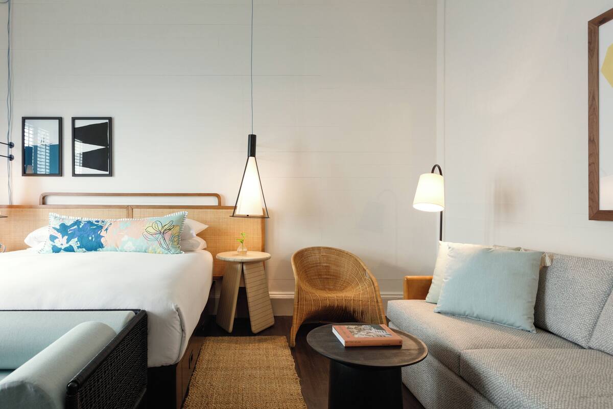 Ett hotellrum med en säng, en soffa, en stol, ett litet bord och ett nattduksbord med en lampa.