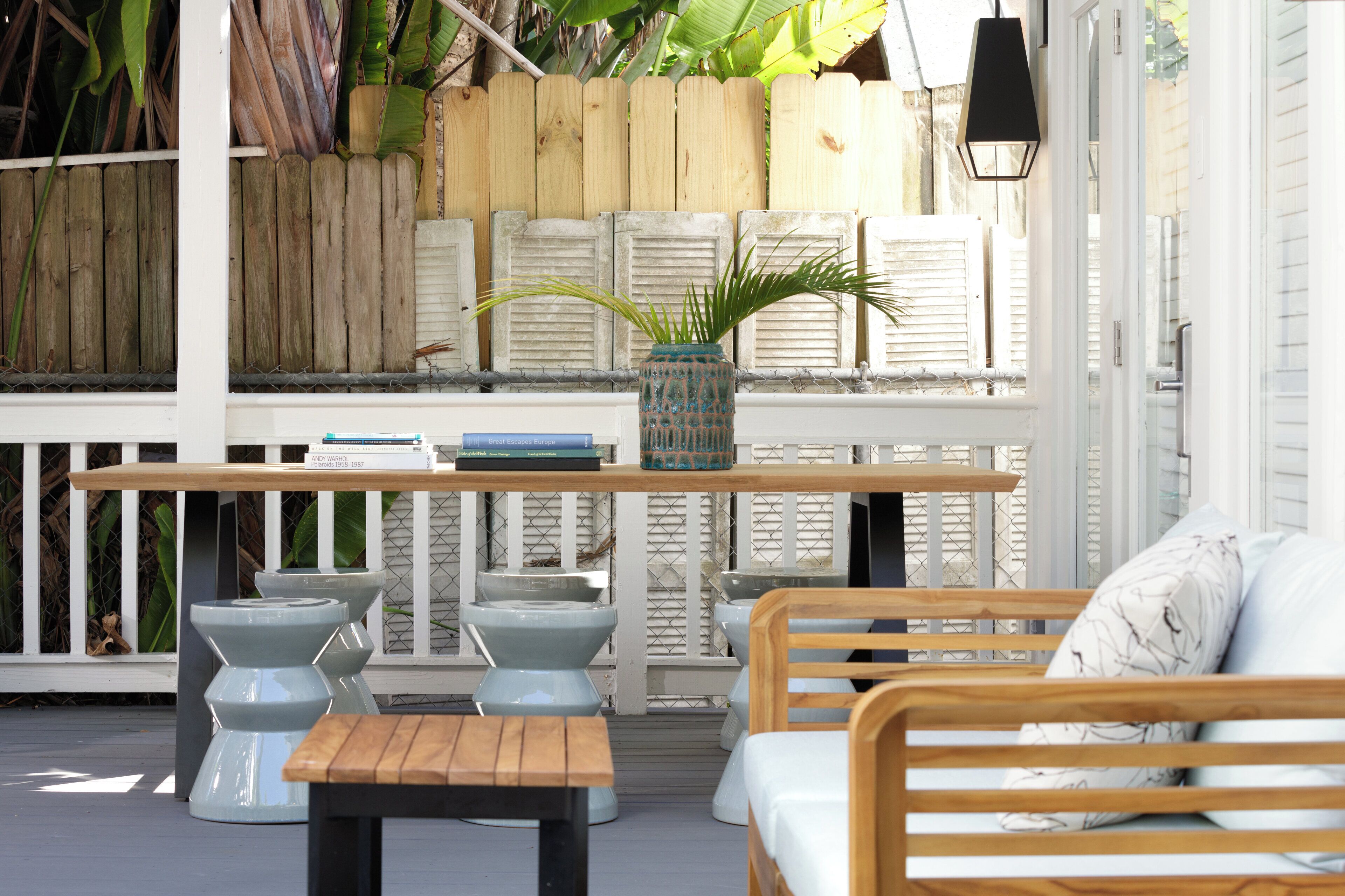 A patio area with a wooden table, two white chairs, a bench, and a white sofa with a cushion.