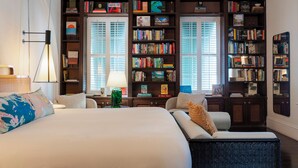 A hotel room with a large bed, a sitting area, and multiple bookshelves filled with books.