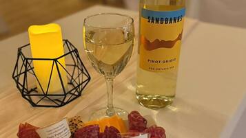 Una mesa con una copa de vino blanco, una botella de Pinot Grigio y una tabla de embutidos, quesos y frutas.