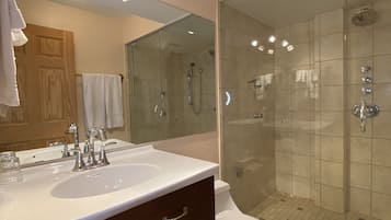 Een moderne badkamer met een wastafelmeubel met dubbele wastafel, een douchecabine met glazen wanden en een toilet.