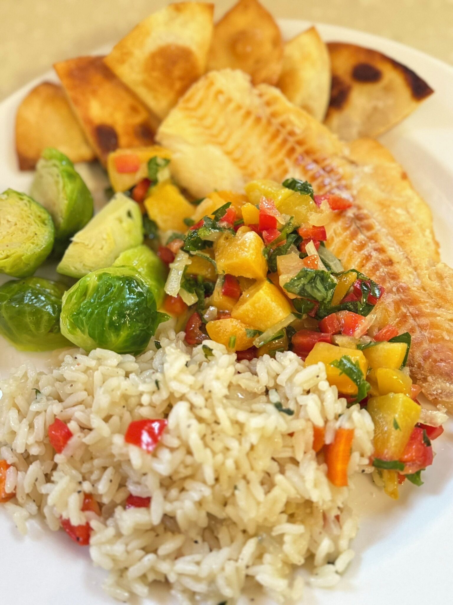 Un plato de comida con un filete de pescado, arroz, coles de Bruselas y una mezcla de verduras.