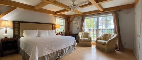 A spacious bedroom with a large bed, two chairs, a ceiling fan, and a window with curtains.