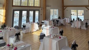 A spacious hall with high wooden ceilings and large windows, furnished with round tables and chairs, suitable for events. - Timber House Resort (Brighton)
