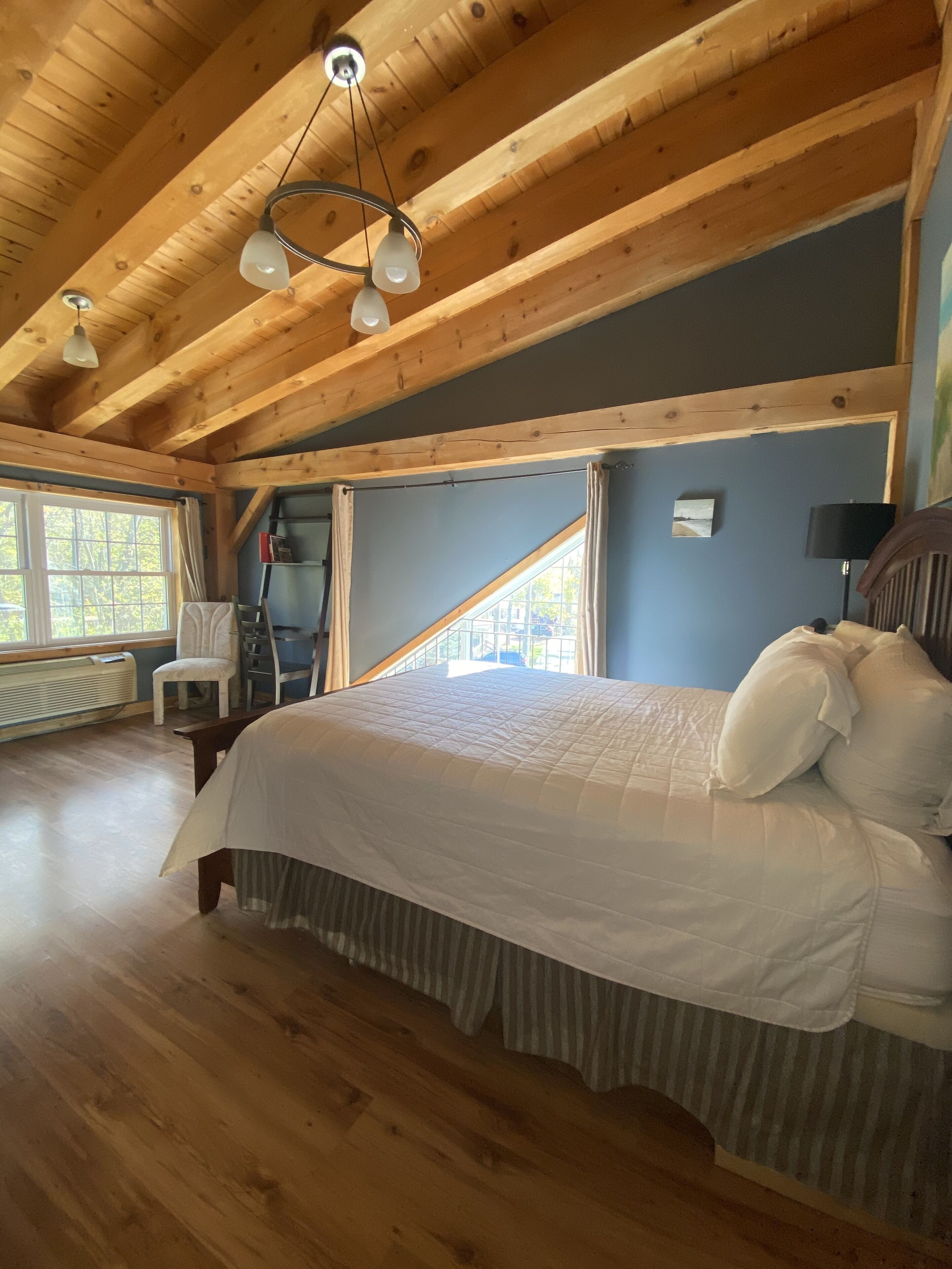 A wooden cabin bedroom with a large bed, a chair, a desk, and a window.