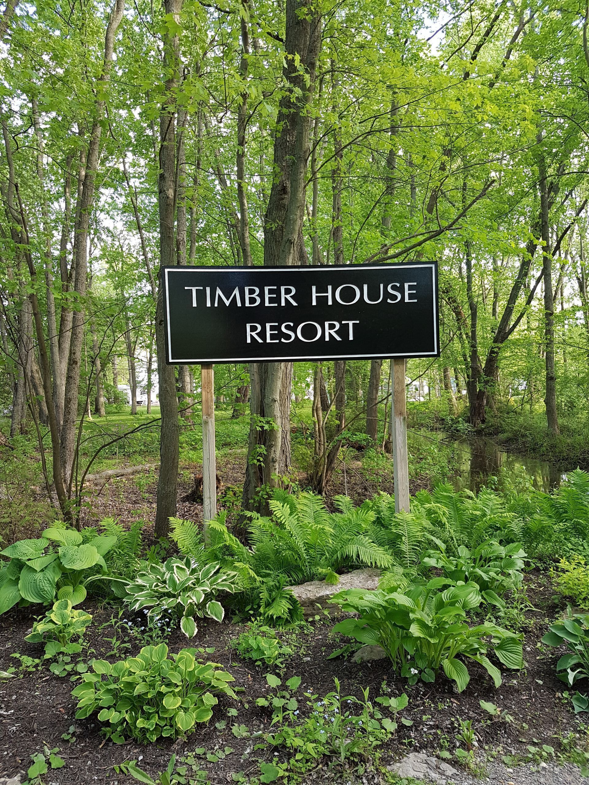 A sign for Timber House Resort surrounded by lush greenery and trees.