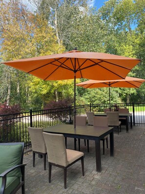 Eine Terrasse im Freien mit Tischen, Stühlen und orangefarbenen Sonnenschirmen, außerdem ein Pflasterboden.
