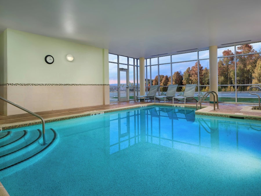 An indoor swimming pool with clear glass walls, a clock, and a view of trees outside.