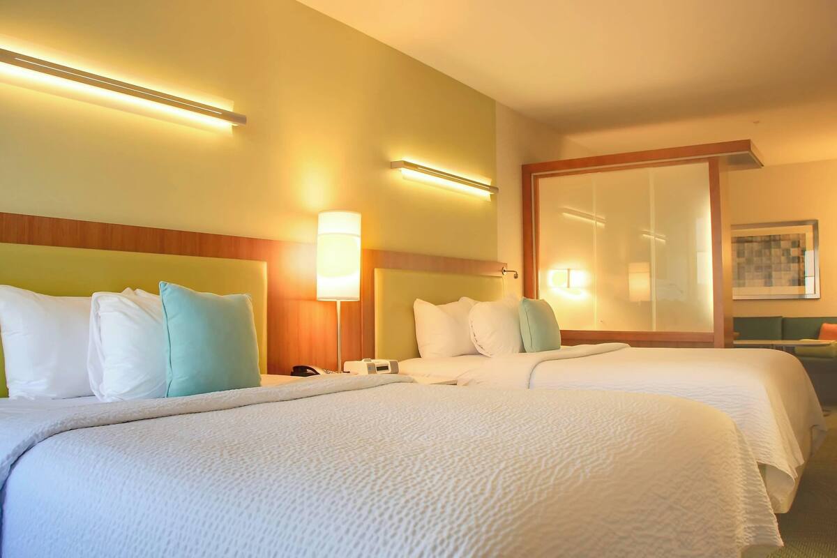 A hotel room with two beds, a nightstand, a lamp, and a large mirror.