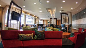 Een moderne lounge met rode banken, een grote flatscreen televisie en meerdere werkplekken.