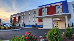 Een modern hotel met een opvallende rode en blauwe gevel, meerdere ramen en een parkeerplaats met auto's.