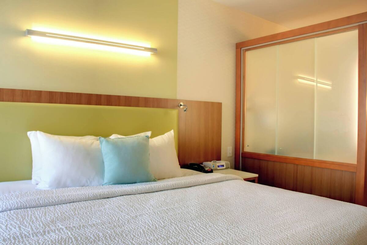 A hotel room with a bed, a nightstand, a lamp, and a wooden headboard.