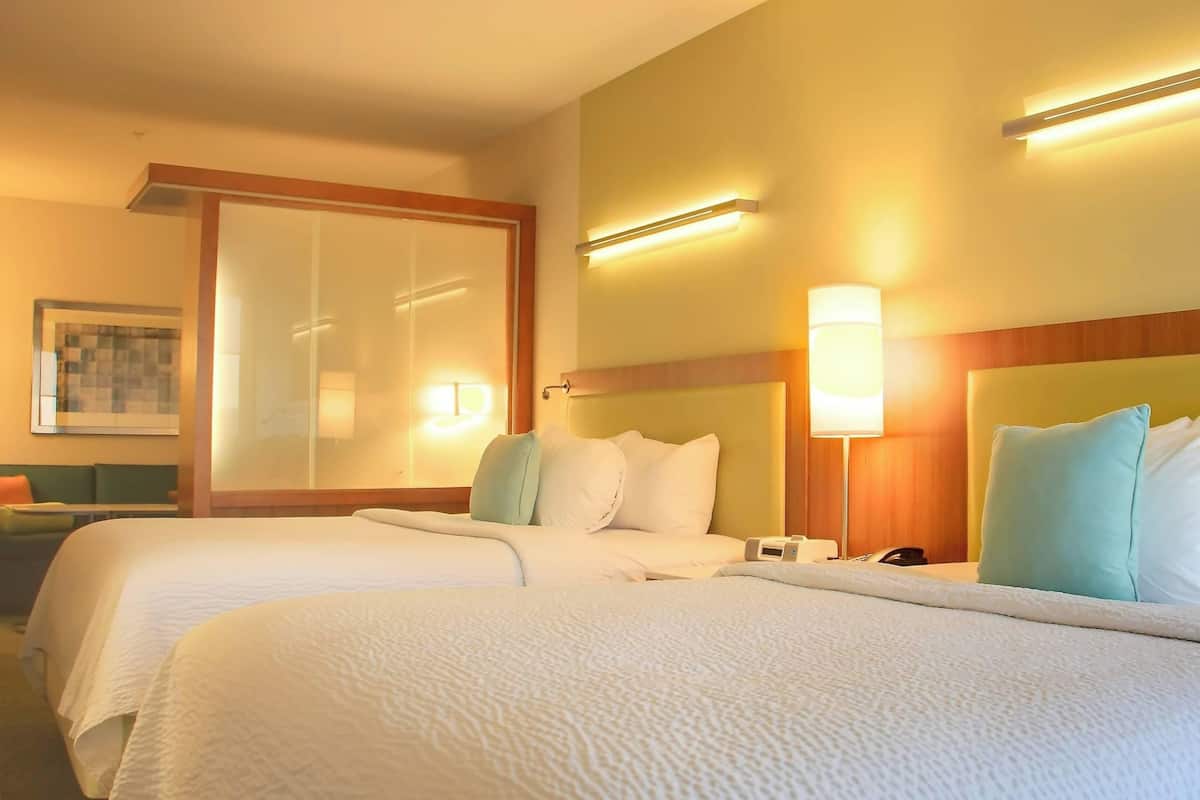 A hotel room with two beds, a large window, and a wall-mounted light fixture.