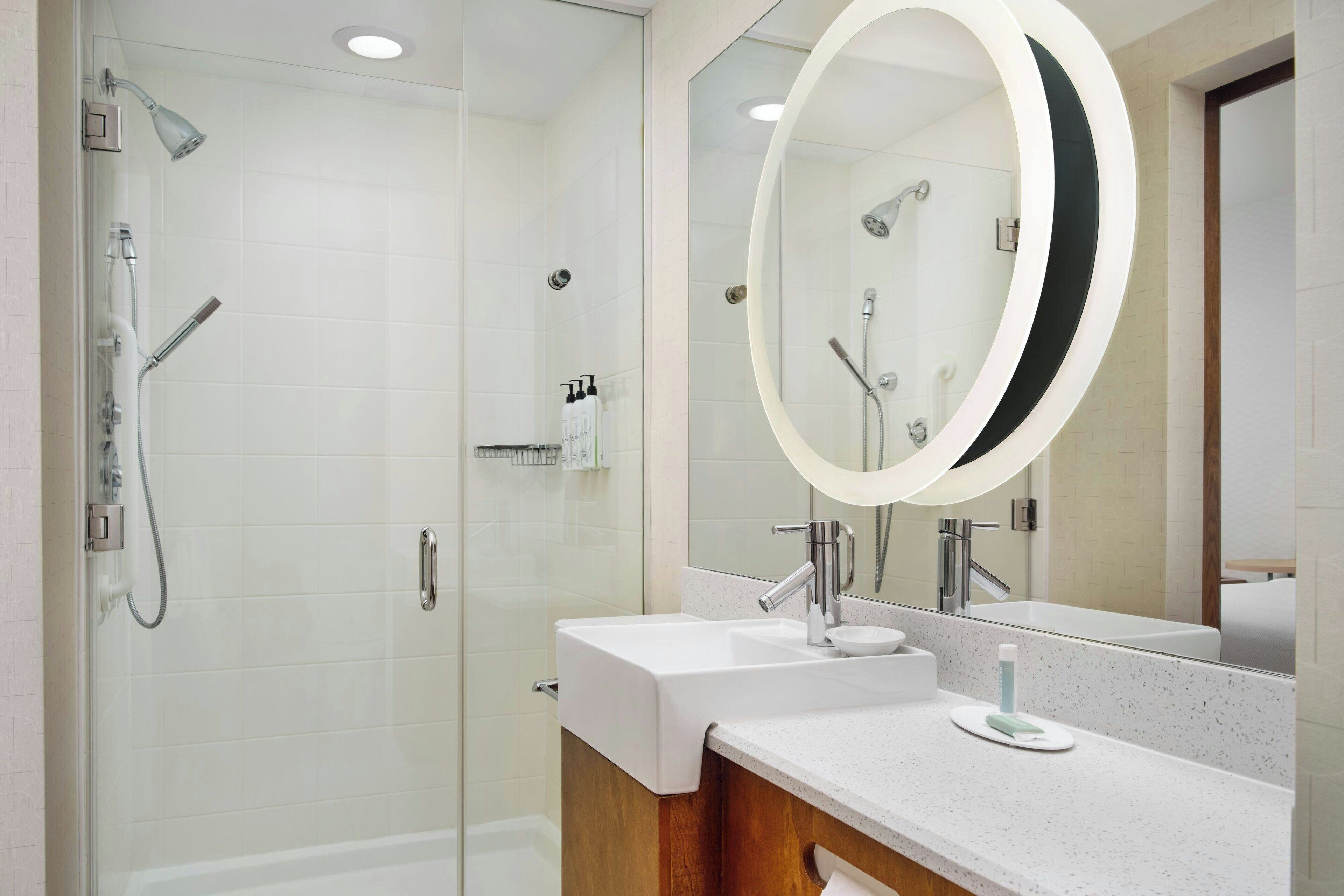 A modern bathroom with a glass-enclosed shower, a large mirror, and a white sink.