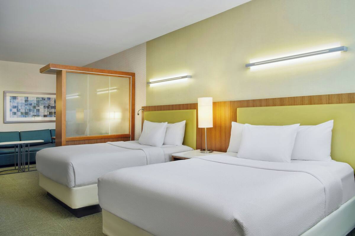 A hotel room with two beds, a sofa, a table, and a wall-mounted TV.