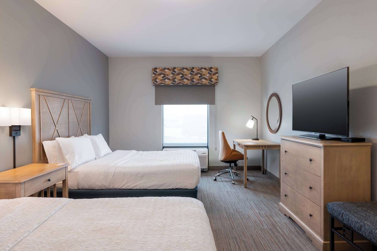 A hotel room with two beds, a desk, a television, and a dresser.