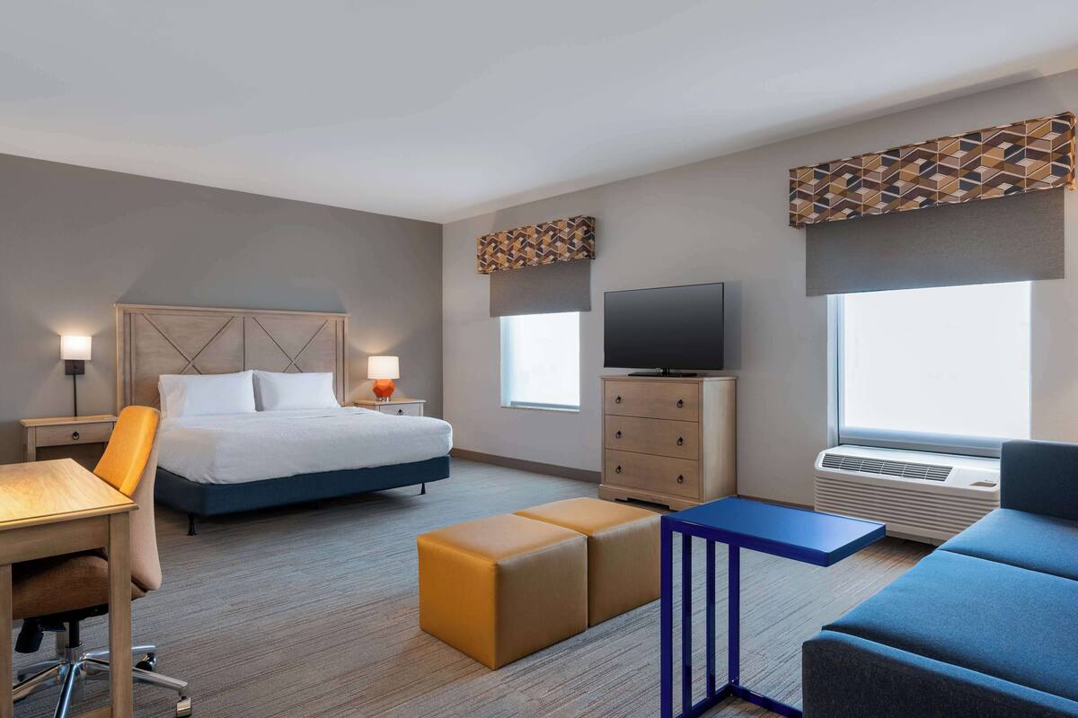 A hotel room with a bed, a desk, a chair, a TV, a dresser, and a sofa.