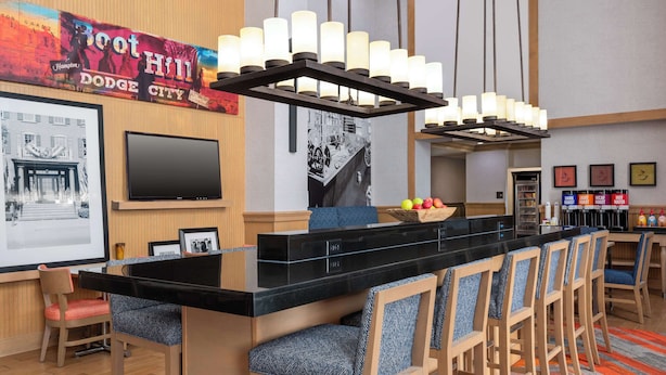 A bar area with a long counter, multiple bar stools, a television, and a large poster on the wall.