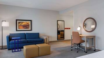 A hotel room with a blue sofa, a small table, a chair, a bed, and a mirror.