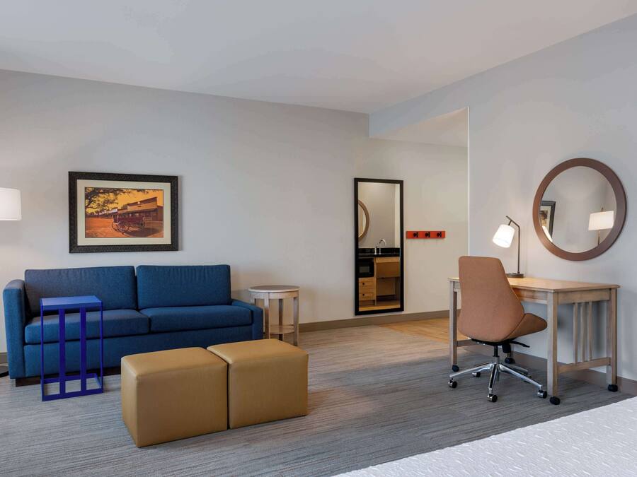 A hotel room with a blue sofa, a small table, a chair, a bed, and a mirror.