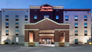 A Hampton Inn & Suites hotel with a modern facade, large windows, and a prominent neon sign.