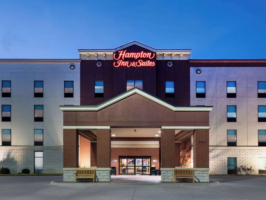 Um hotel Hampton Inn & Suites com fachada moderna, janelas amplas e um letreiro de neon chamativo.