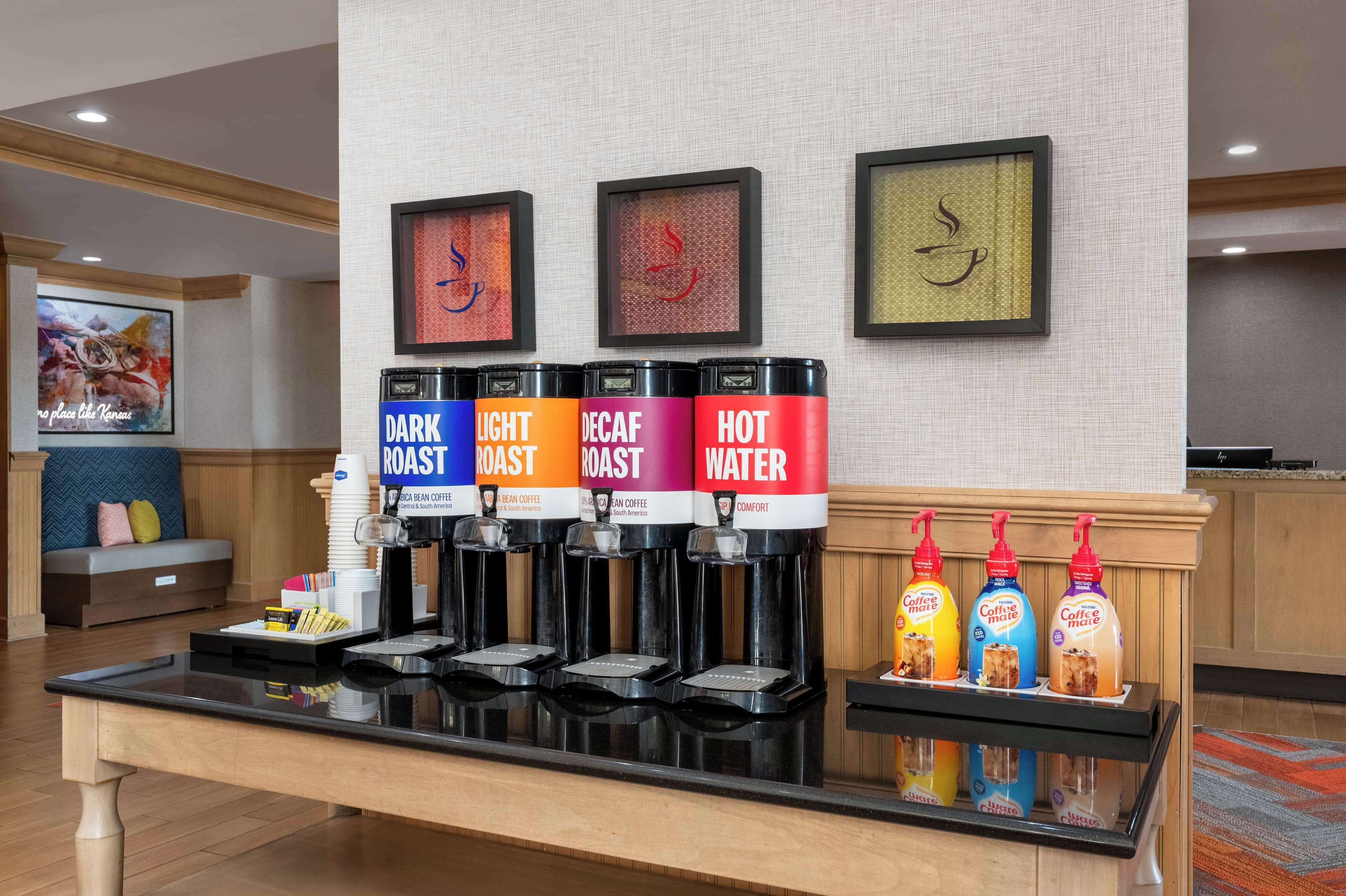 Un espace dédié au café, équipé de quatre distributeurs étiquetés « MÉLANGE CORSÉ », « MÉLANGE LÉGER », « MÉLANGE DÉCAFÉINÉ » et « EAU CHAUDE ». On y trouve également trois bouteilles d’arômes pour café, étiquetées « CAFÉ MÂLE », « CAFÉ MÂLE » et « CAFÉ MÂLE ».