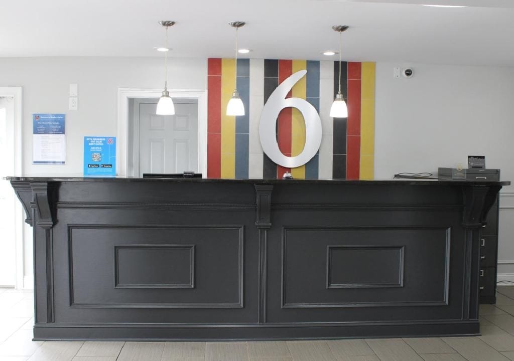 Un mostrador de recepción con un gran número 6 en la pared, una puerta blanca y un cartel informativo azul.