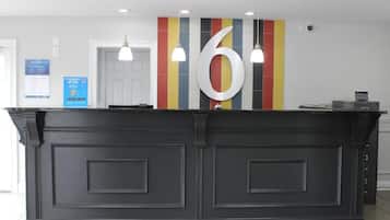 Un mostrador de recepción con un gran número 6 en la pared, una puerta blanca y un cartel informativo azul.