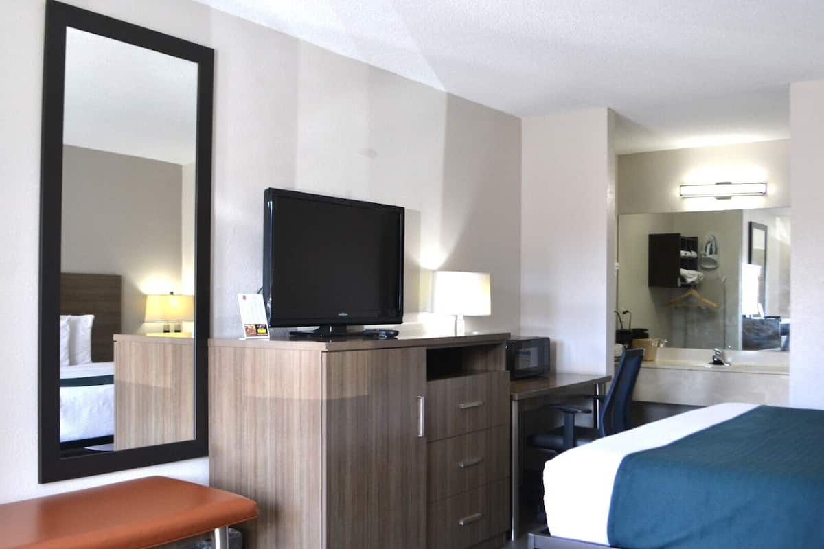 Ein Hotelzimmer mit Bett, Schreibtisch mit Computer, Fernseher, Spiegel und angrenzendem Badezimmer.
