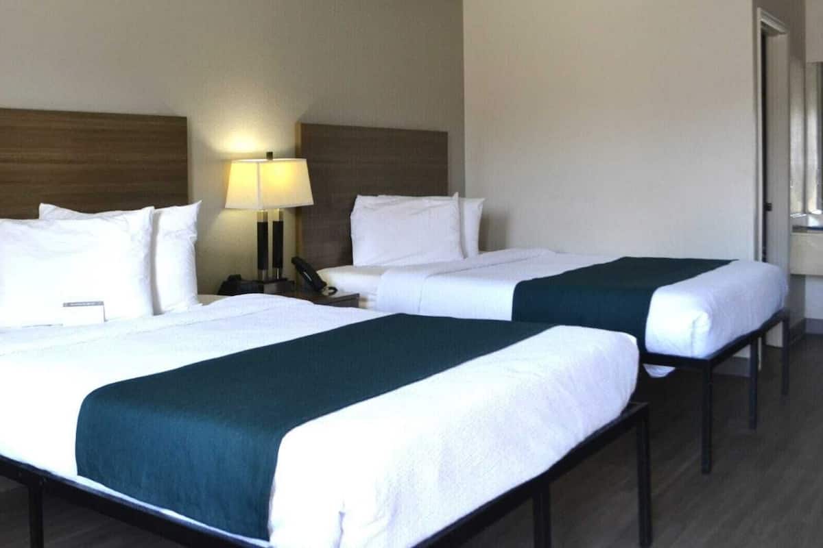 Ein Hotelzimmer mit zwei Betten, einem Nachttisch mit Lampe und einem Fenster.