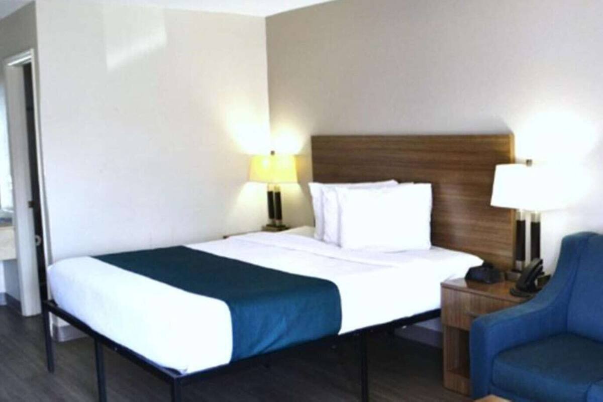 Ein Hotelzimmer mit einem Doppelbett, zwei Nachttischlampen, einem blauen Sofa und einem Holz-Kopfschild.