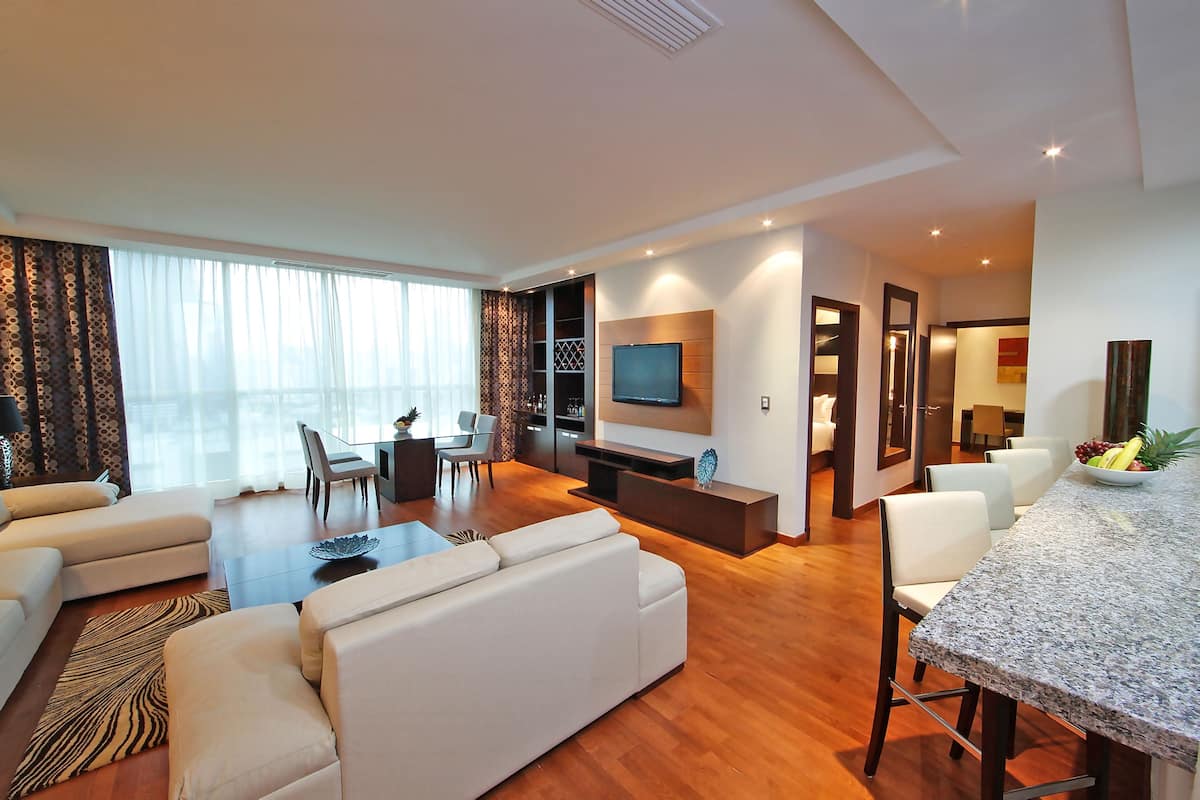 A modern living room with a sofa, a dining table, and a TV mounted on the wall.