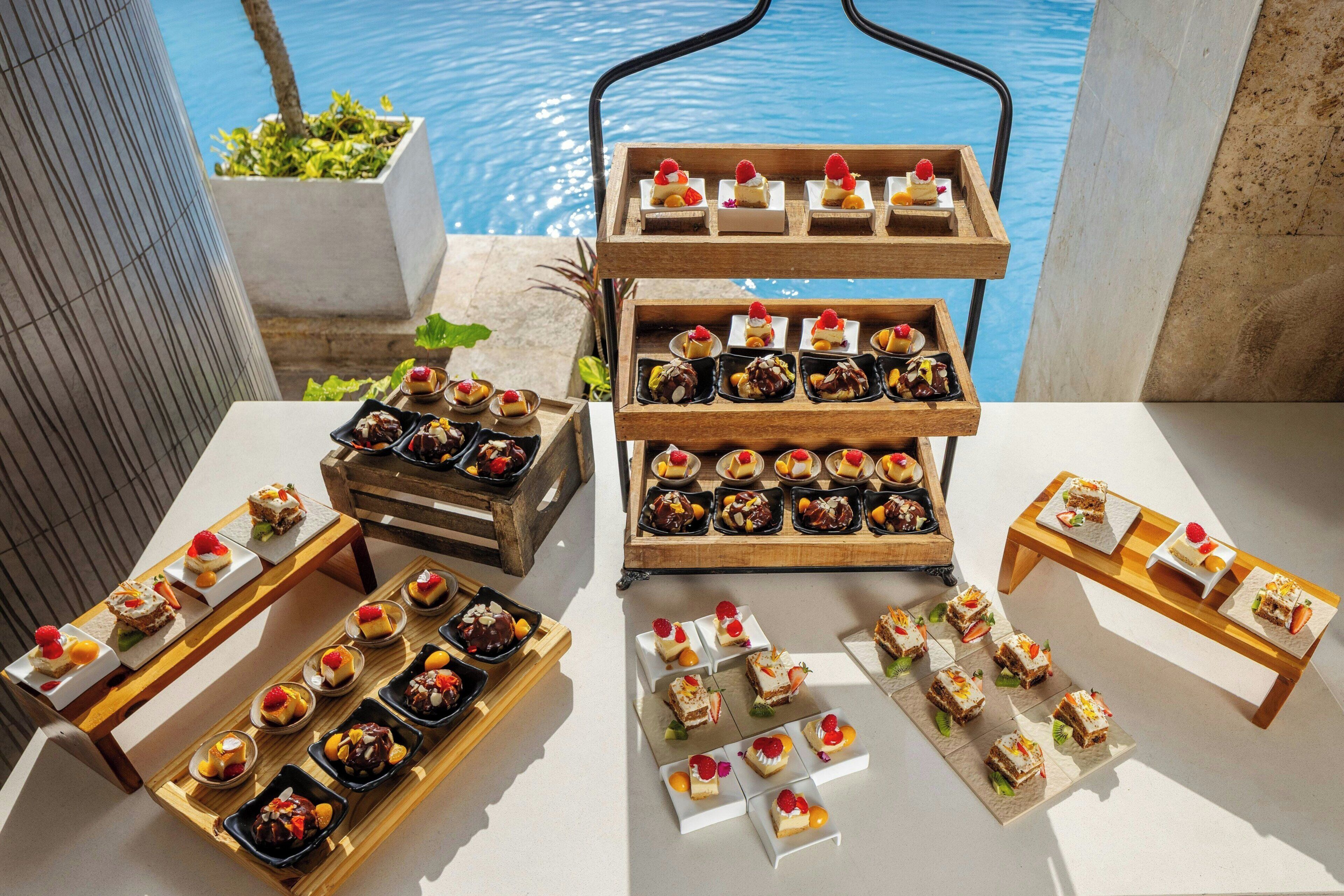 Une variété de desserts disposés sur des tables et des plateaux près d’une piscine.