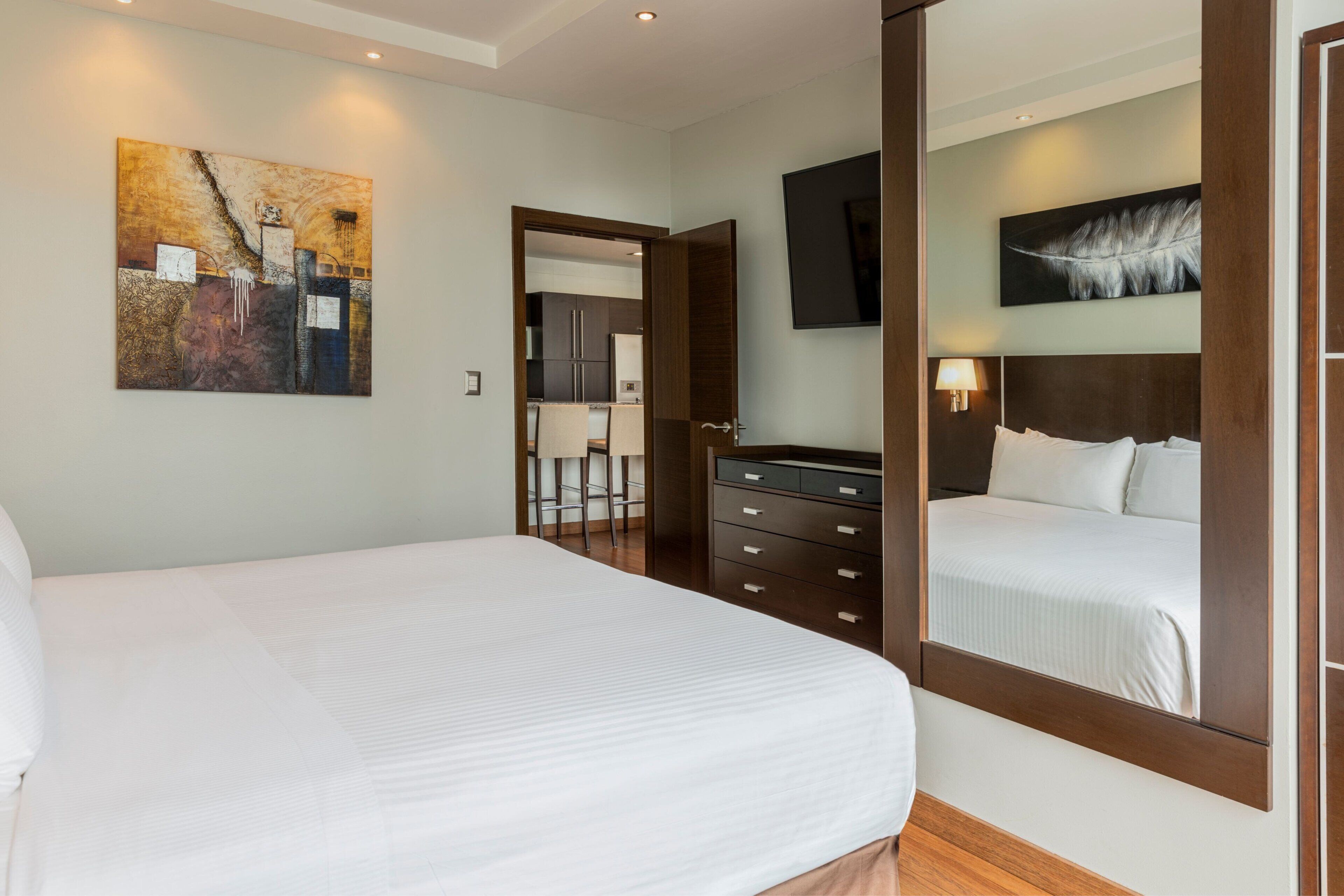 Una camera d'albergo con un letto grande, una cassettiera, uno specchio, un quadro e una televisione.
