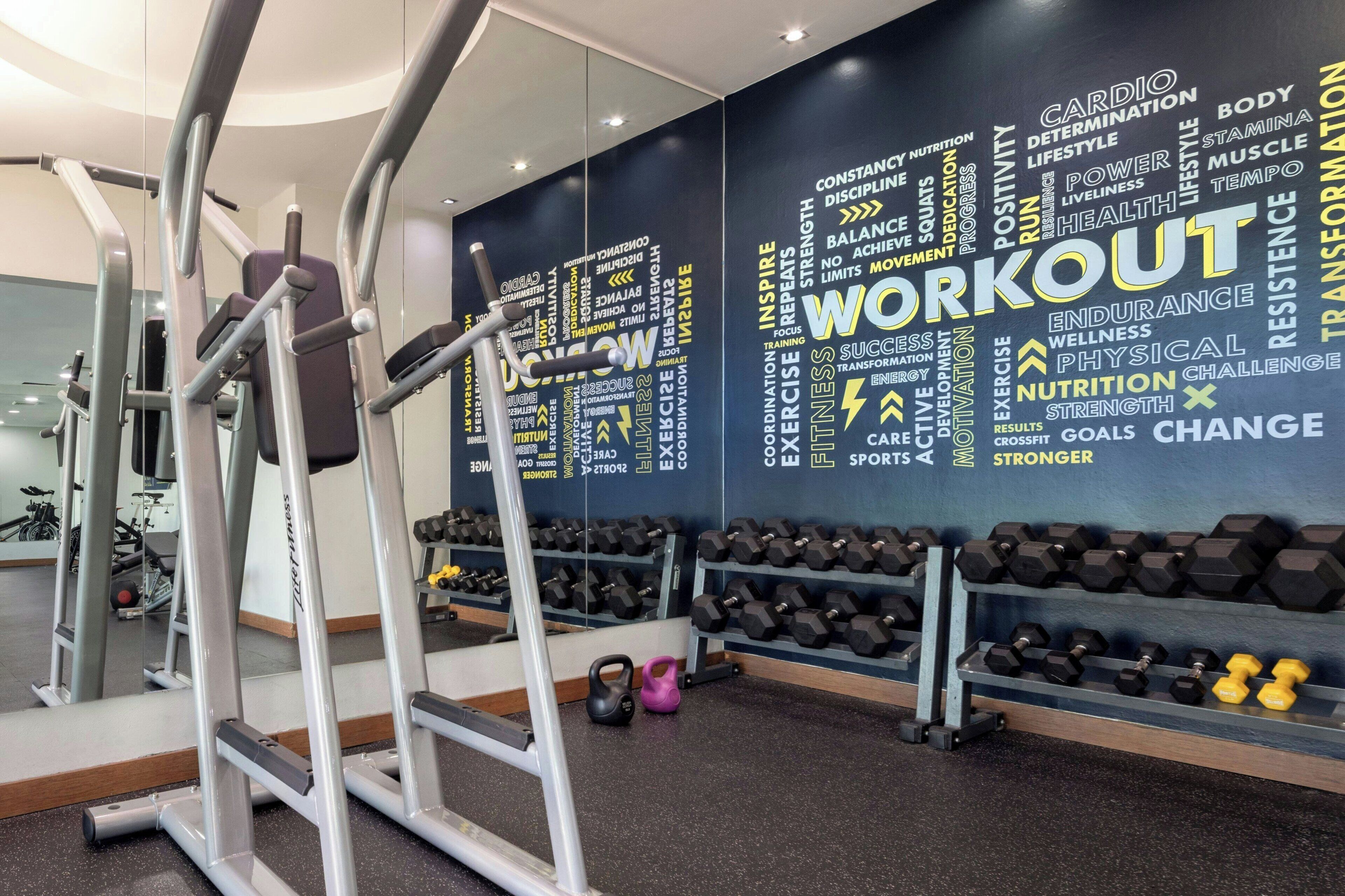 A gym with exercise equipment, a wall with motivational words, and a rack of dumbbells.