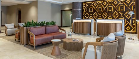 Een moderne lobby met een bank, fauteuils, een bijzettafeltje en een receptiebalie.