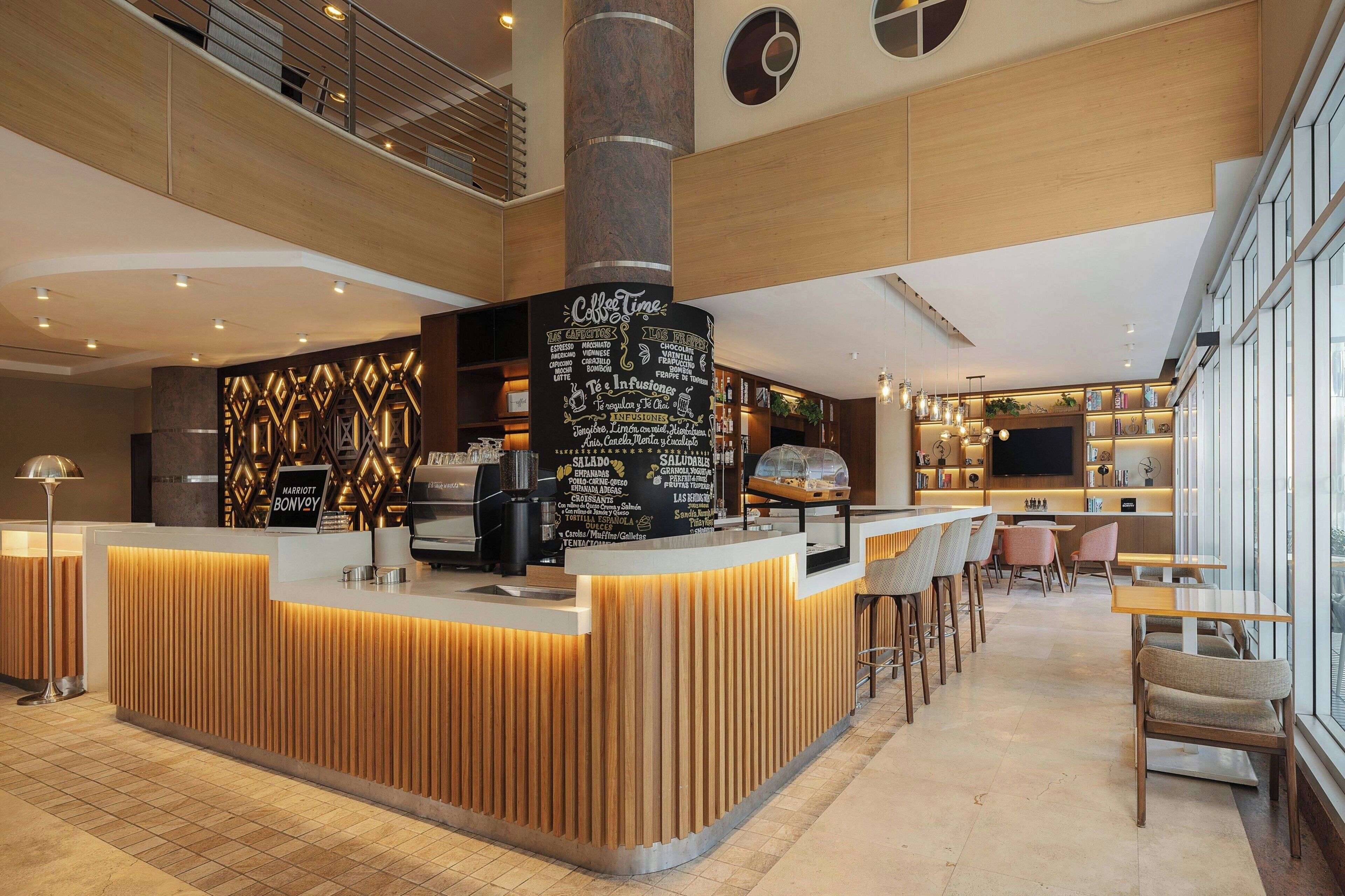A modern hotel lobby with a central reception desk, seating area, and a large window providing a view.