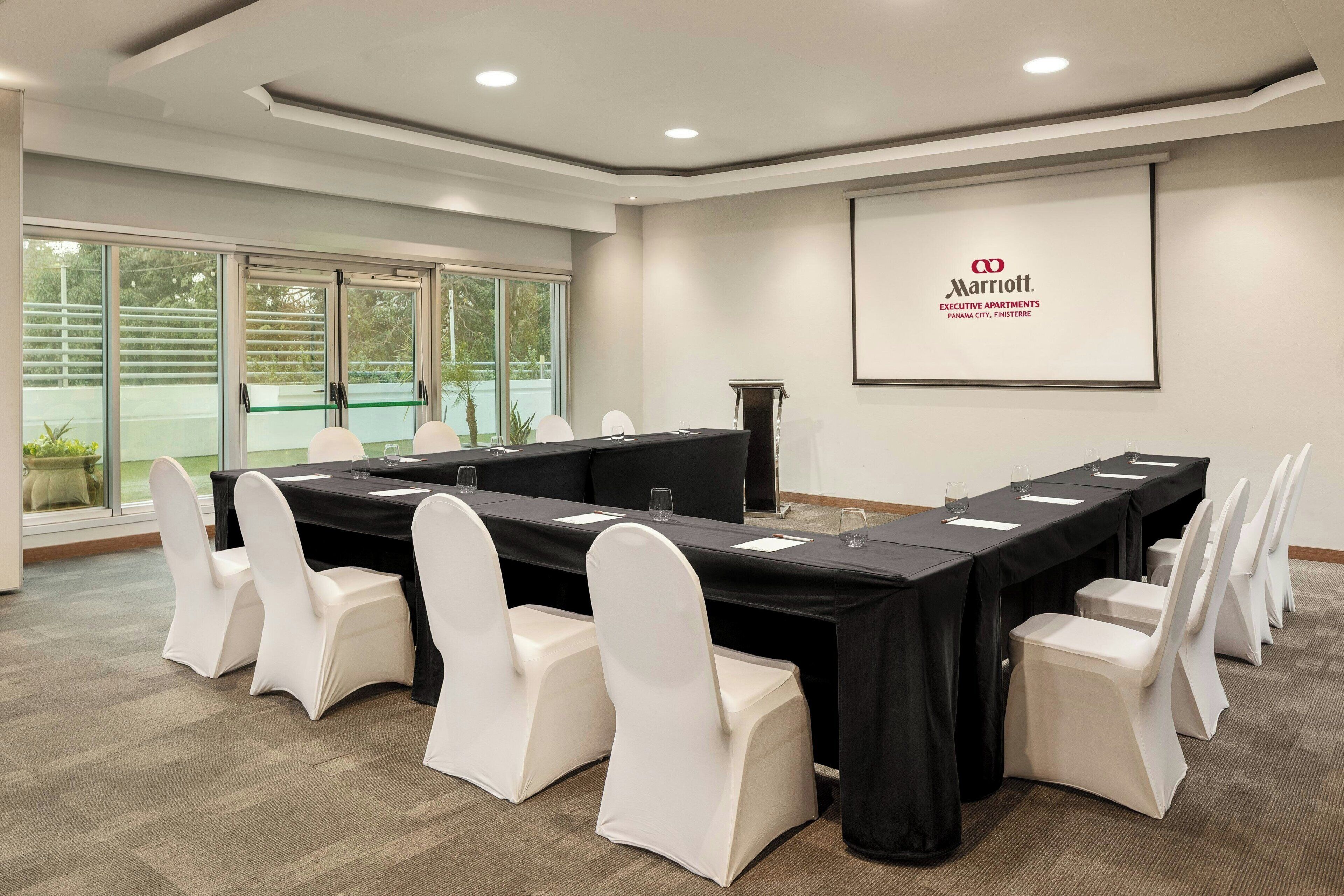 A conference room with a long table, white chairs, and a projector screen displaying the Marriott logo.
