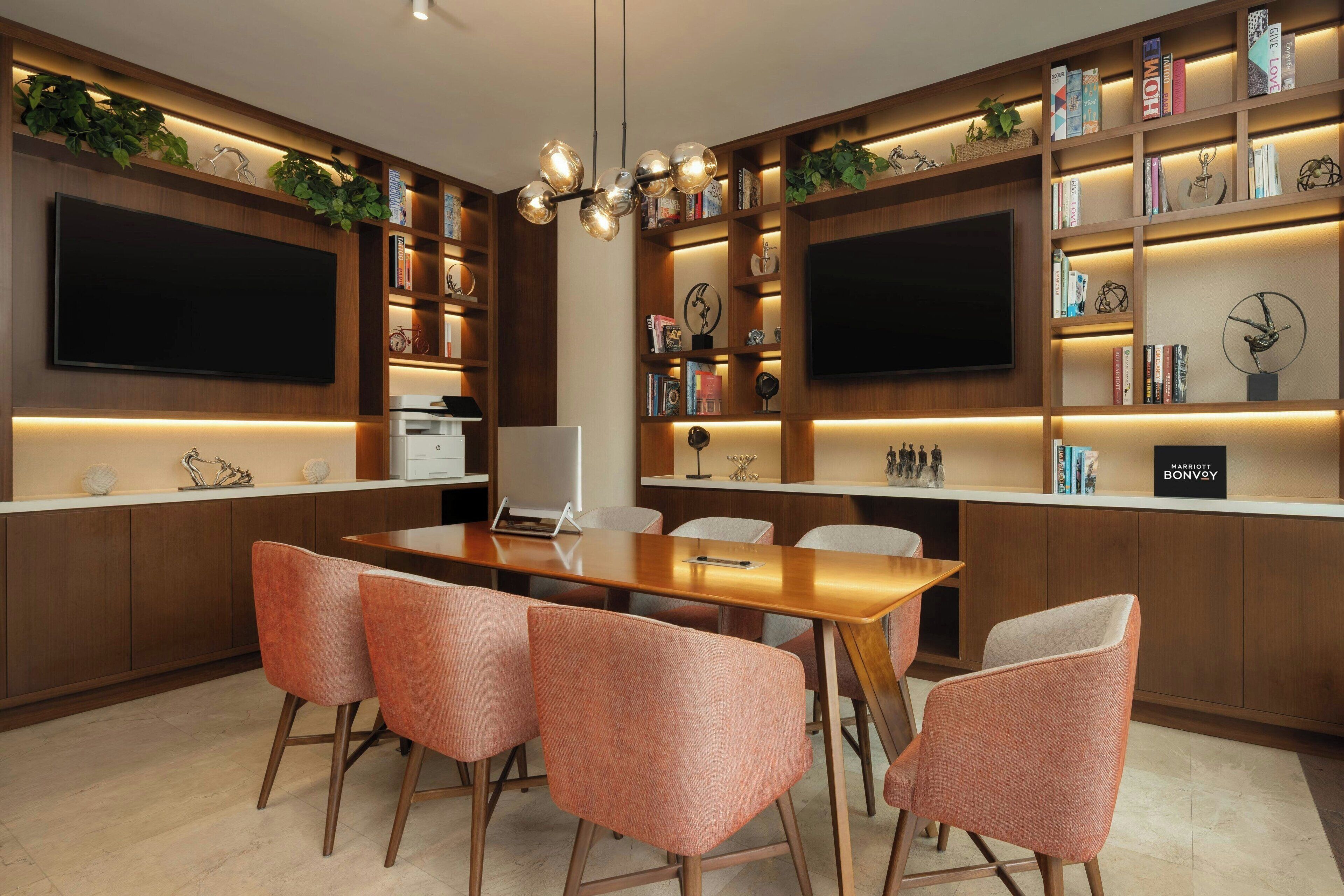A modern kitchen with a wooden table, four chairs, built-in bookshelves, and two large flat-screen TVs.