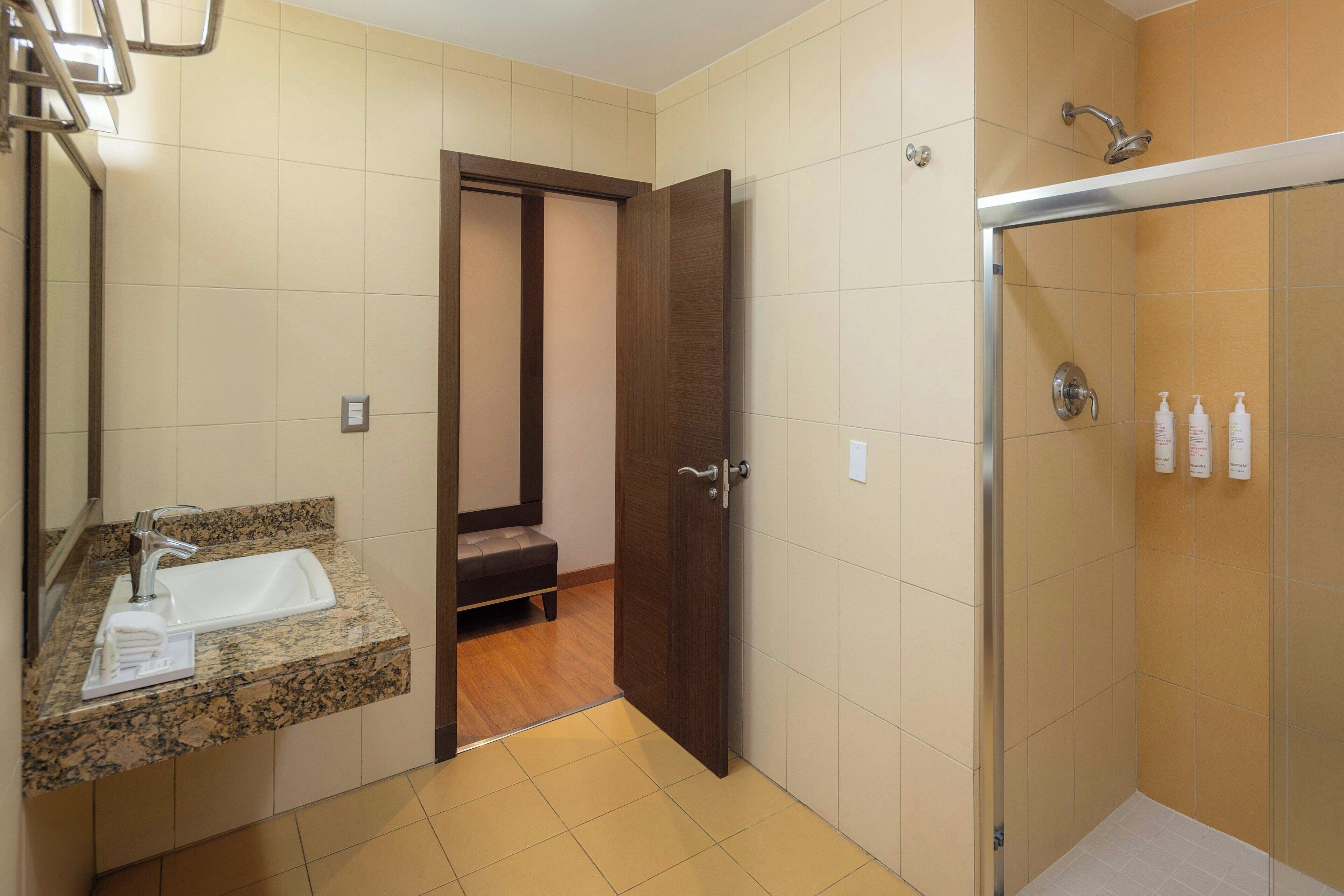 Un bagno con lavandino, specchio, doccia e una porta che dà su un corridoio.